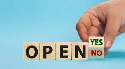 The word OPEN is written on wooden cubes. The hand turns the wooden cube and changes the word NO OPEN to YES OPEN