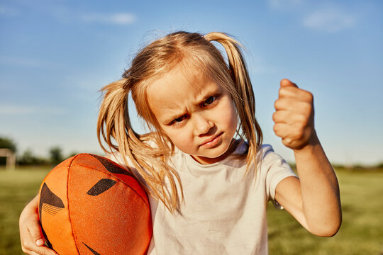 Blond girl holding rugby ball gesturing fist on sunny day