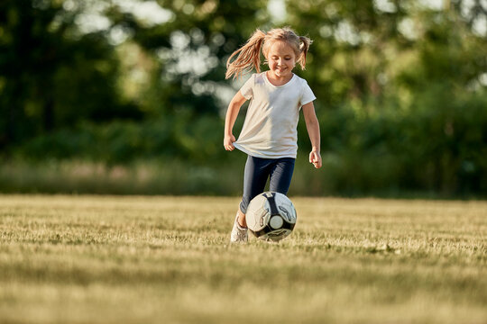 Happy blond girl playing soccer at sports field