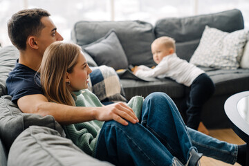 Young white man and woman with little son sitting on sofa at home