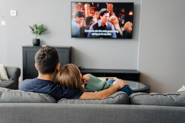 Young white man and woman sitting on sofa and watching TV at home