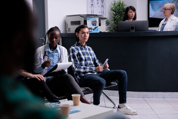 African american doctor talking with patients at hospital reception checking appointments and...