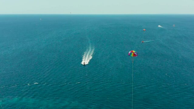 People flying on a colorful parachute towed by a motor boat, aerial view. Parasailing in blue sky.