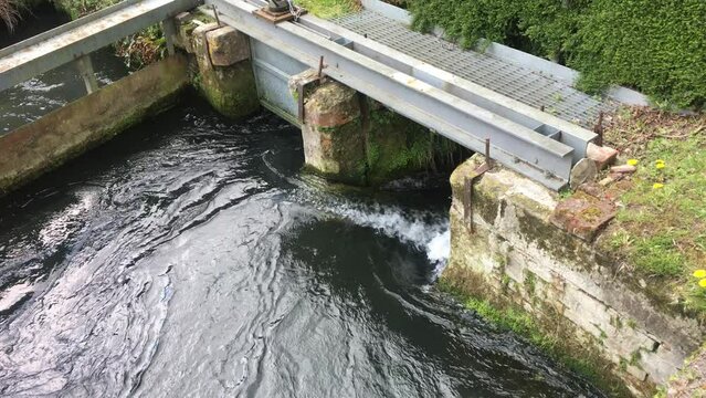 Flood waters push up against an open sluice gate on a fast flowing freshwater stream in an area of farmland
