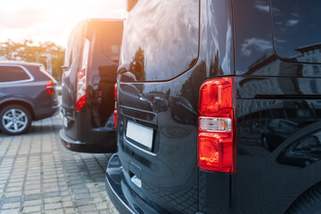 Close-up detail tail light view of many modern luxury black vans parked in row at car sale rental leasing dealer against sunset. Commericial trasfer cargo transportation company fleet. Vip charter