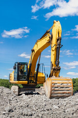 Powerful industrial excavator in a quarry against a blue cloudy sky. Loading crushed stone and soil with an excavator. Earth-moving equipment and earthworks.