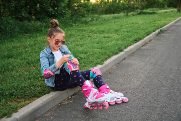 Pretty little girl learning to roller skate on beautiful summer day in a park.
