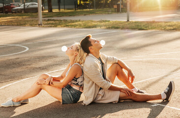 summer holidays and people concept - happy young couple sitting back to back and blowing bubble...