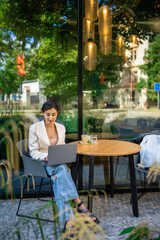 Young smiling brunette business woman in stylish smart dress working on laptop in cafe at street of Prague