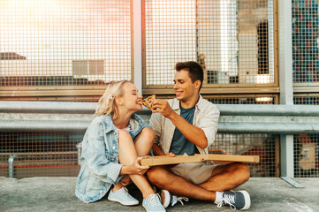 summer holidays, food and people concept - happy young couple eating takeaway pizza on city roof...