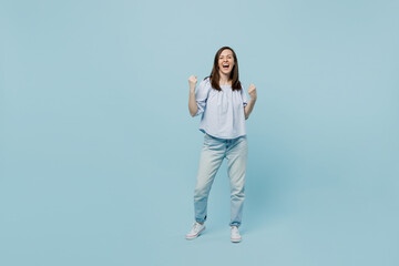 Full body young happy woman she 20s wears casual blouse doing winner gesture celebrate clenching fists say yes isolated on pastel plain light blue background studio portrait. People lifestyle concept.