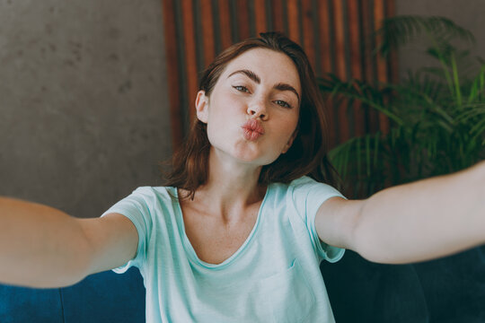 Close up young happy woman she 20s in casual clothes mint t-shirt do duckface selfie shot pov on mobile cell phone sit on blue sofa indoor rest at home in own room apartment People lifestyle concept.