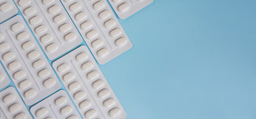 Pharmaceutical medication and medicine pills in packs on blue background. White pills in blister...