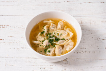 dumplings with meat filling and broth. on a white wooden background