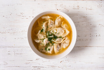 dumplings with meat filling and broth. on a white wooden background