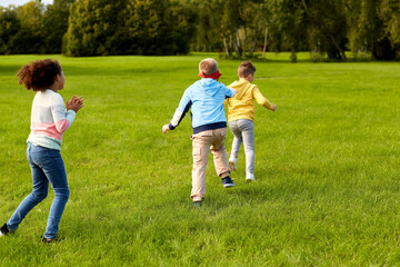 childhood, leisure and people concept - group of happy children playing tag game and running at park