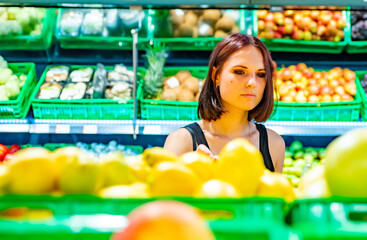 Young woman choosing lemon while shopping in supermarket.