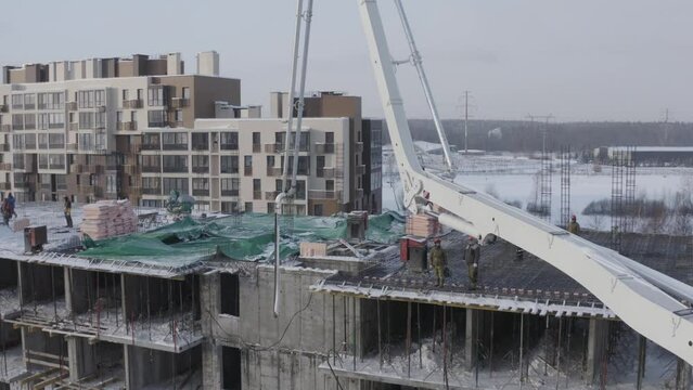 A drone view of the construction of a residential building using a concrete pump. Workers are building a house on a sunny winter day.