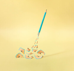 Creative composition with wooden waste from sharpened pencil against gold yellow background. Surreal knowledge concept.
