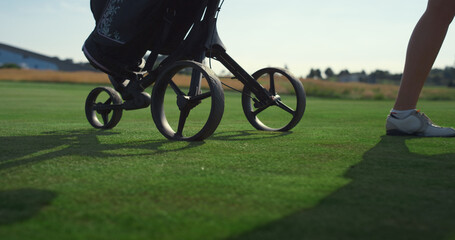 Golfer carry sport equipment trolley clubs bag. Golf player legs walk on course.