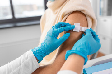 Fototapeta premium medicine, health and vaccination concept - close up of doctor or nurse applying medical patch to vaccinated woman in mask at hospital