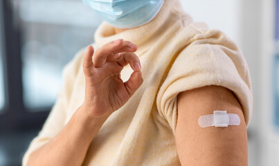 medicine, health and vaccination concept - close up of vaccinated senior woman with medical patch on arm showing ok gesture at hospital