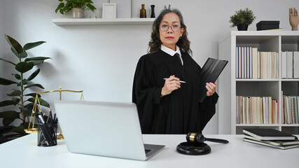 Senior female in robe gown uniform holding document and looking confidently to camera. Lawyer, justice and law, attorney, concept