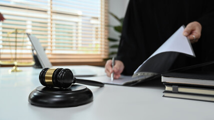 Gavel putting on white table and professional female lawyer signing papers in background. Lawyer,...