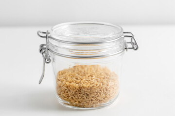 food storage, healthy eating and diet concept - close up of jar with brown rice on white background