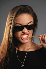 Portrait of a girl with sunglasess holding a chain with a pendant in her teeth. Creative advertising