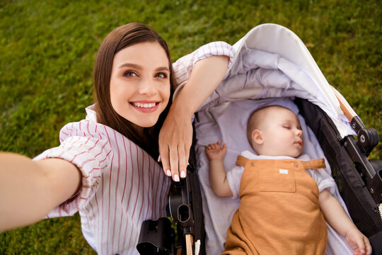 Photo of charming cute positive mommy blogger walk sleeping infant kid pram make selfie portrait outside
