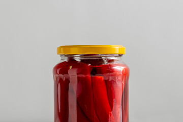 food, storage and preserve concept - close up of jar with pickled red hot chili peppers on grey background