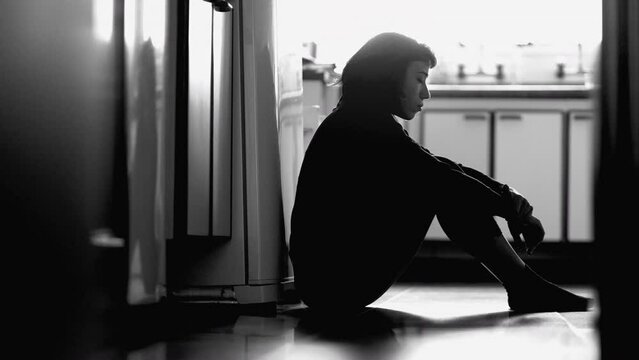 Depressed girl sitting on kitchen floor on monochrome. Black and white photography of woman in desperate moment
