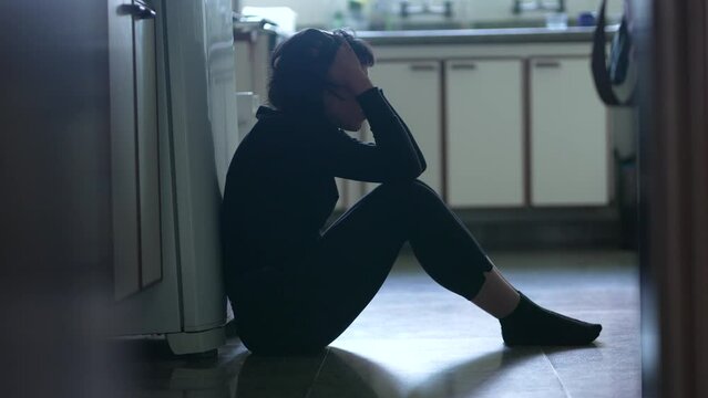 Depressed young woman sitting on kitchen floor feeling desperate in difficult times suffering from mental illness