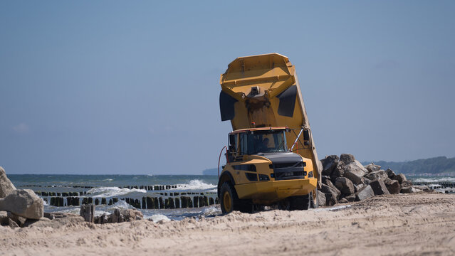 KOLOBRZEG, WEST POMERANIAN - POLAND - 2022: A big vehicle carries boulders on the sea beach 
