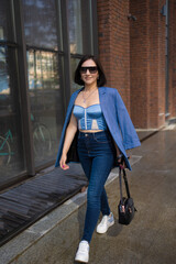brunette girl in a blue jacket and jeans walks through the city streets