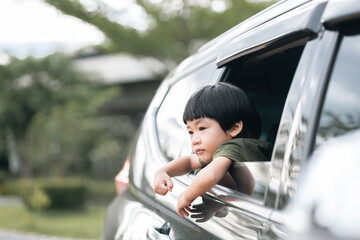 Happy asian boy waving hands gesturing hello out of the car window during a trip with his family. Little child sticking head outta the windshield traveling in a car on a summer vacation.