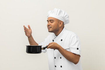Smiling Young man chef in uniform gesture smelling empty hot pot stew soup delicious dish menu good...