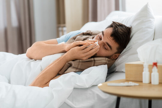 people and health problem concept - unhappy sick man blowing nose lying in bed at home