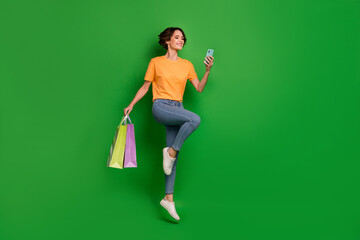 Full length portrait of active cheerful girl hold packages telephone jump isolated on green color background