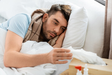 people and health problem concept - unhappy sick man lying in bed at home and taking paper tissue...
