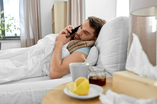 health, illness and people concept - sick man calling on smartphone in bed at home
