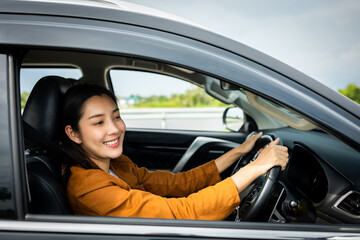 Obraz na płótnie Canvas Young beautiful asian women getting new car. she very happy and excited. Smiling female driving vehicle on the road on a bright day.