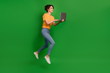 Fototapeta na wymiar Full length profile portrait of pretty active person jump arms hold use netbook write email isolated on green color background