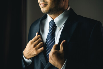 Confident businessman adjust classic blue suit with necktie near window in hotel room. Handsome man...