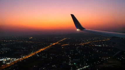 aircraft wing in the sky with sunset sky and city light background,fly to travel concept,romantic...