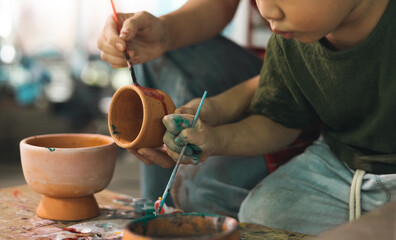 Fototapeta na wymiar Happy family moment Mother teaching son how to painting mug cup ceramic workshop. Child creative activities and art. Kid playing pottery workshop. Developing children's learning skills.