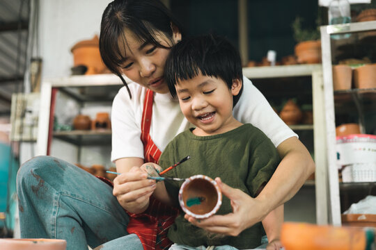 Happy family moment Mother teaching son how to painting mug cup ceramic workshop. Child creative activities and art. Kid playing  pottery workshop. Developing children's learning skills.
