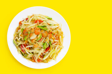 Dish of spicy papaya salad on yellow background.