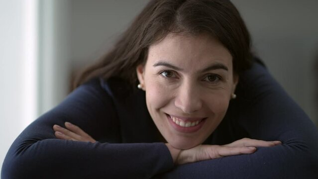 Portrait of woman in her 30s smiling at camera leaning on table with arms crossed closeup face